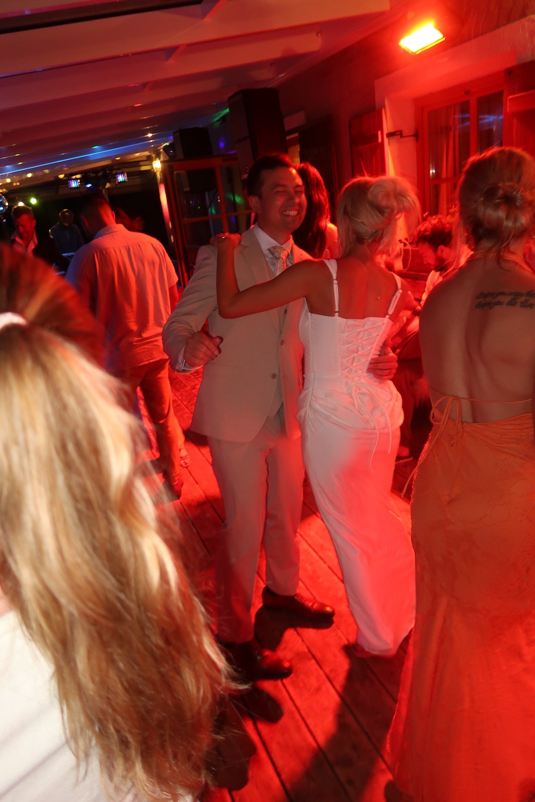 Bride and groom dancing together, her lace-up corset dress visible from behind, DJ speaker and string lights in the background at an Italian reception.