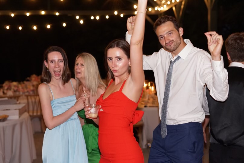 High-energy candid of guests dancing in formal attire at outdoor reception, one with fist raised.